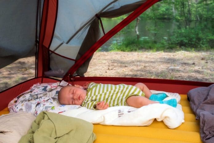 Cute baby boy tourist is sleeping in a tent in summer time outdoors